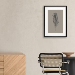May include: A framed print of a black and white illustration of a feather on a light brown background.