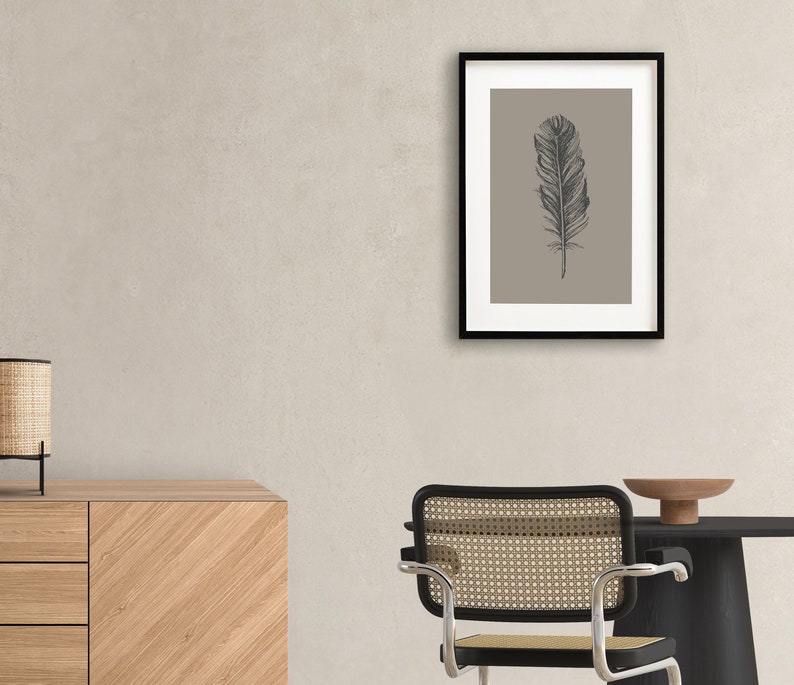 May include: A framed print of a black and white illustration of a feather on a light brown background.