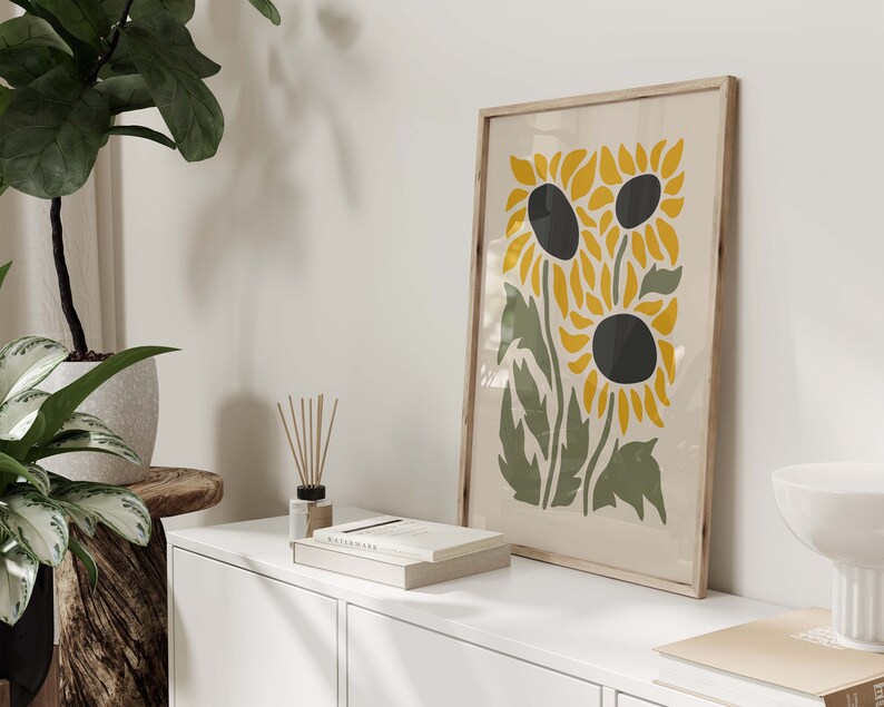 May include: A framed print of a stylized illustration of three sunflowers with yellow petals and black centers on a cream background.