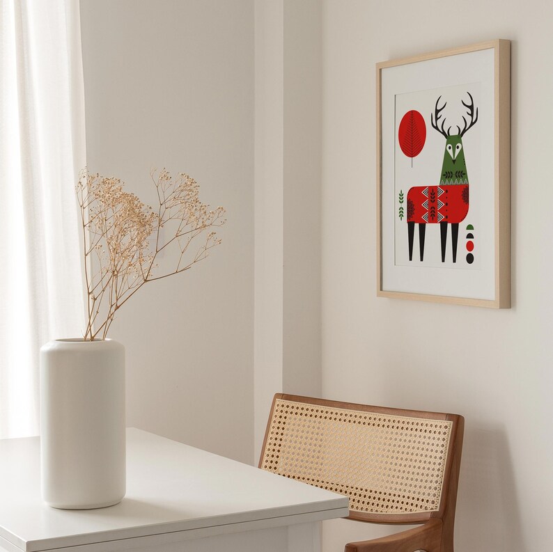 May include: A framed print of a stylized deer with red, green, and black geometric patterns. The deer is standing on a white background with a red circle and a green tree in the background.