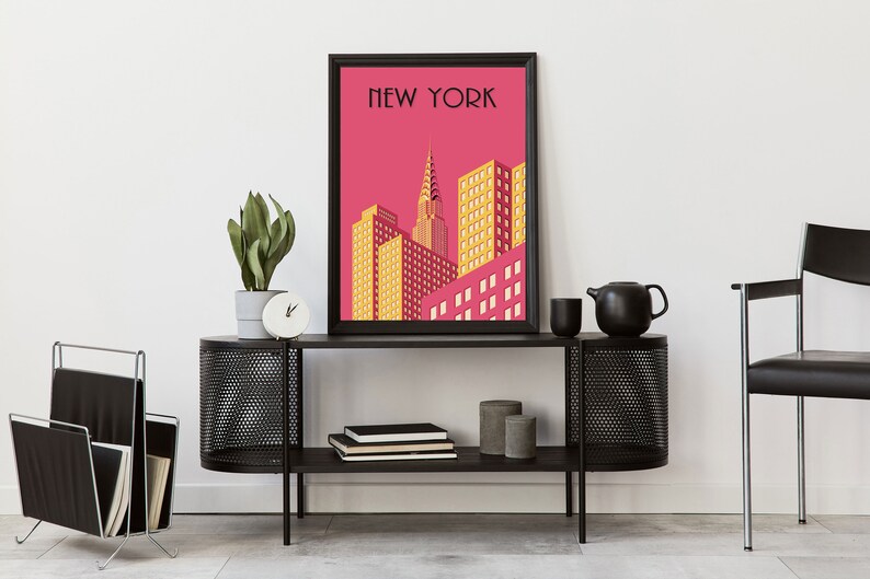 Puede incluir: Un p&oacute;ster enmarcado en negro con fondo rosa y una ilustraci&oacute;n amarilla y roja del horizonte de la ciudad de Nueva York. El p&oacute;ster dice "NEW YORK" en texto negro en la parte superior. El p&oacute;ster est&aacute; colgado en una pared blanca sobre una estanter&iacute;a de metal negro con un revistero negro a la izquierda y una tetera de cer&aacute;mica negra a la derecha.