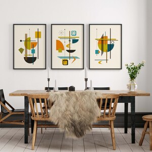 Puede incluir: Tres impresiones de arte abstracto enmarcadas con formas geom&eacute;tricas en tonos de amarillo, naranja, azul, verde y marr&oacute;n. Las impresiones est&aacute;n colgadas en una pared blanca sobre una mesa de comedor de madera con dos sillas y una manta de piel.