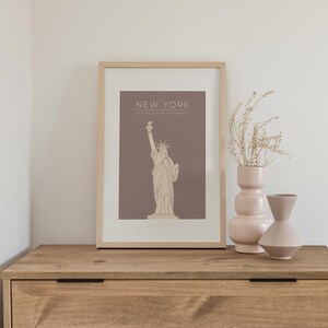 May include: A framed print with a brown background and a line drawing of the Statue of Liberty. The text "NEW YORK" and "UNITED STATES OF AMERICA" is printed in beige below the image.