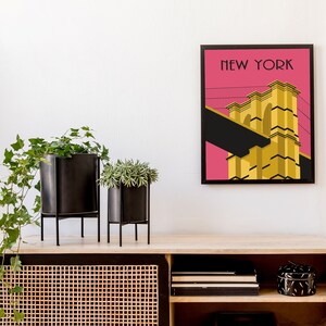 Puede incluir: Una impresi&oacute;n enmarcada de un puente amarillo sobre un fondo rosa con el texto "NEW YORK" en la parte superior. La impresi&oacute;n est&aacute; colgada en una pared blanca sobre un estante de madera con plantas y objetos decorativos.
