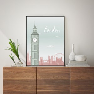May include: A framed art print featuring a stylized illustration of London's skyline. The artwork showcases Big Ben, the London Eye, and other landmarks in shades of gray and pink against a light blue background. The word "London" is written in a cursive font.