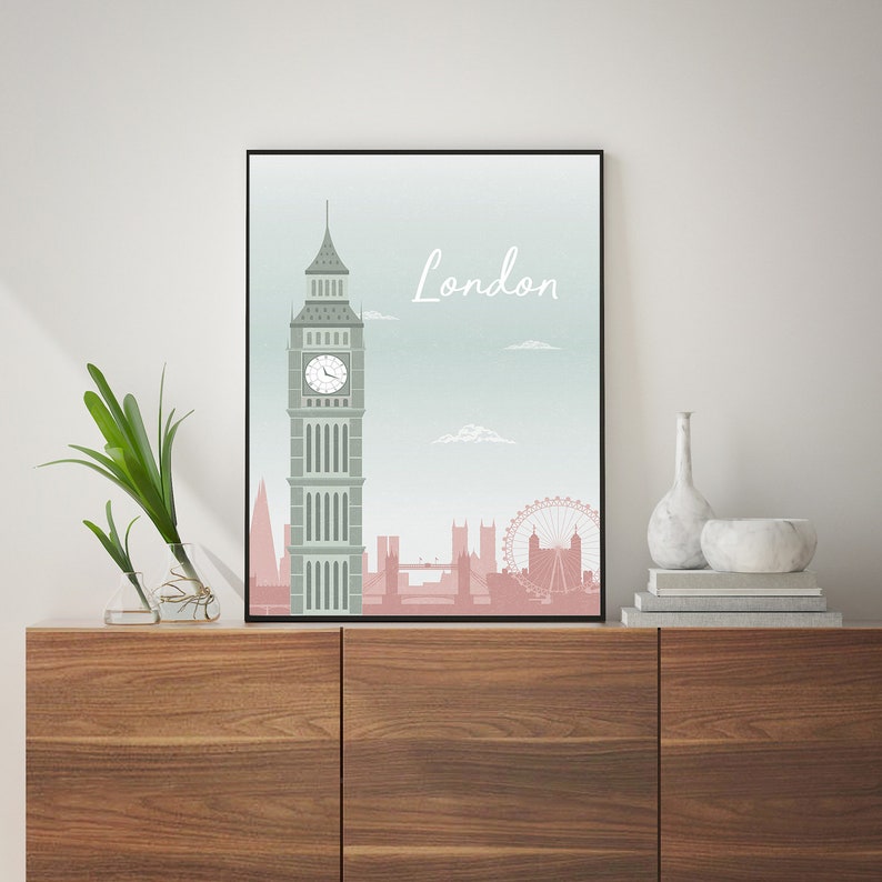May include: A framed art print featuring a stylized illustration of London's skyline. The artwork showcases Big Ben, the London Eye, and other landmarks in shades of gray and pink against a light blue background. The word "London" is written in a cursive font.