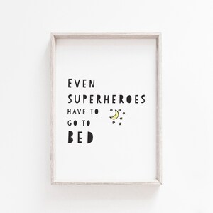 Puede incluir: Una impresi&oacute;n enmarcada con el texto "Incluso los superh&eacute;roes tienen que irse a la cama" en texto negro con una luna creciente amarilla y estrellas.