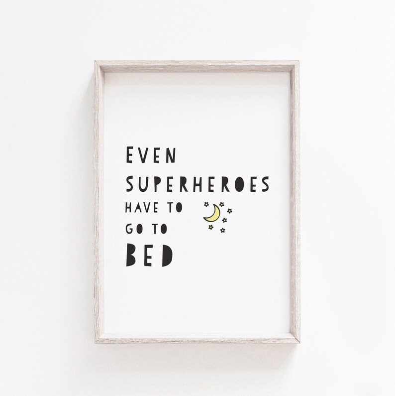 Puede incluir: Una impresi&oacute;n enmarcada con el texto "Incluso los superh&eacute;roes tienen que irse a la cama" en texto negro con una luna creciente amarilla y estrellas.