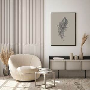 May include: A beige armchair with a round back and a swivel base sits in a living room with a light wood floor. A small square table with a stack of books sits in front of the chair. A shelf with books and decorative items sits on the wall behind the chair. A framed print of a black and white feather on a beige background hangs on the wall.