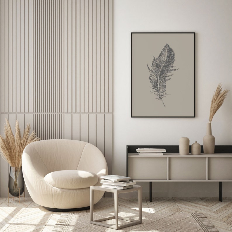 May include: A beige armchair with a round back and a swivel base sits in a living room with a light wood floor. A small square table with a stack of books sits in front of the chair. A shelf with books and decorative items sits on the wall behind the chair. A framed print of a black and white feather on a beige background hangs on the wall.