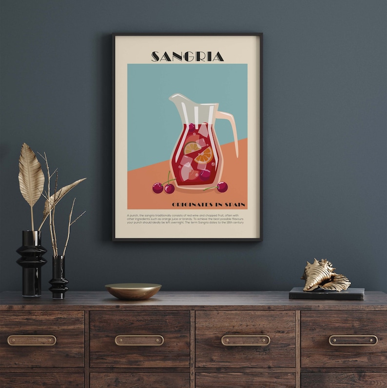 May include: A framed art print featuring a Sangria illustration. The artwork depicts a pitcher filled with red wine, fruit, and ice. Text at the top reads "SANGRIA," with "ORIGINATES IN SPAIN" below. The print is displayed on a wooden cabinet.