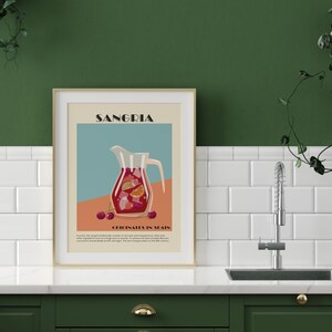 May include: A framed art print featuring a Sangria illustration. The image shows a pitcher filled with red liquid and fruit slices, with the word "SANGIRA" at the top. The text "ORIGINATES IN SPAIN" is also visible.
