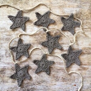 May include: A string of gray crocheted stars on a rustic wooden background. The stars are connected by a white twine.