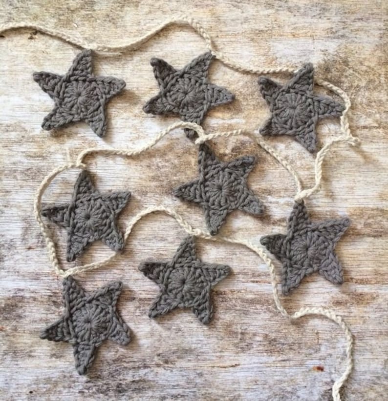 May include: A string of gray crocheted stars on a rustic wooden background. The stars are connected by a white twine.