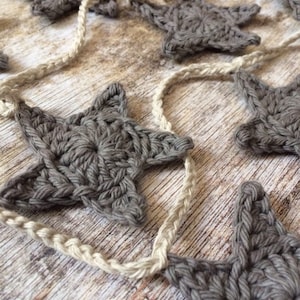 May include: A garland of crocheted gray stars strung together with natural twine. The stars are a simple design with five points and a textured surface.