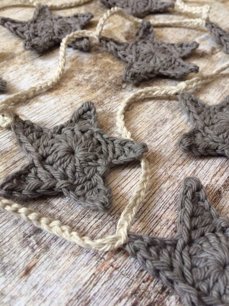 May include: A garland of crocheted gray stars strung together with natural twine. The stars are a simple design with five points and a textured surface.