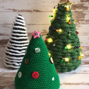 May include: Three crocheted Christmas trees, one with white and green stripes, one with green and white buttons, and one with green and colorful lights.