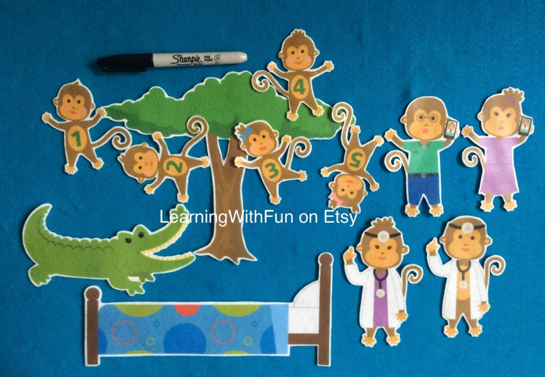 K&ouml;nnte beinhalten: Ein Set aus Filz-Ausschnitten f&uuml;r ein Kinderspiel. Das Set enth&auml;lt einen gr&uuml;nen Alligator, einen braunen Baum mit f&uuml;nf Affen, zwei &Auml;rzte, einen Affen-Mama und einen Affen-Papa und ein Bett. Der Text "LearningWithFun on Etsy" ist auf den Baum gedruckt.