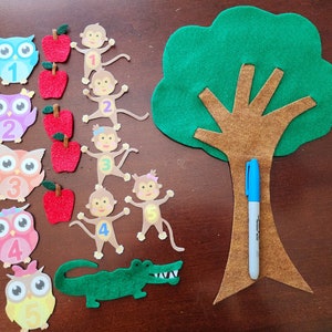 May include: A felt craft set for learning numbers. The set includes a green felt tree with a brown trunk, five owls with numbers 1-5, five monkeys with numbers 1-5, and red felt apples.