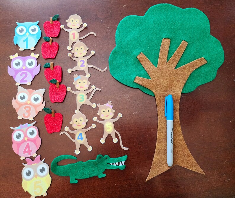May include: A felt craft set for learning numbers. The set includes a green felt tree with a brown trunk, five owls with numbers 1-5, five monkeys with numbers 1-5, and red felt apples.