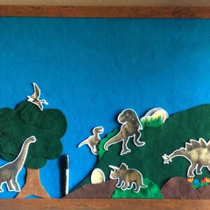 May include: A blue felt board with a green felt tree, brown felt hills, and various dinosaur cutouts. The dinosaurs are a pterodactyl, a brachiosaurus, a velociraptor, a tyrannosaurus rex, a triceratops, and a stegosaurus.