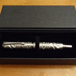 May include: A silver pen with a textured design is displayed in a black velvet-lined box.