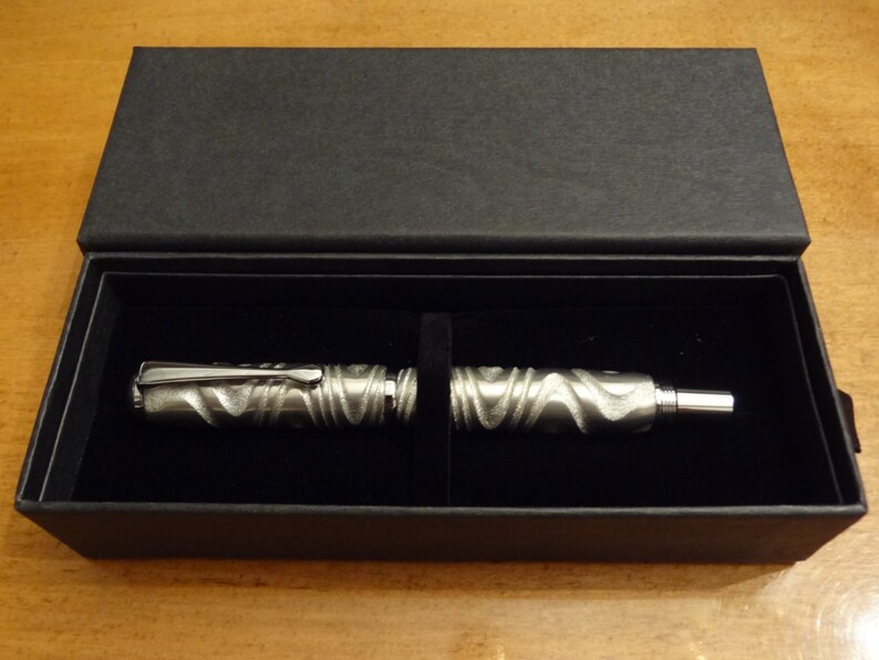 May include: A silver pen with a textured design is displayed in a black velvet-lined box.