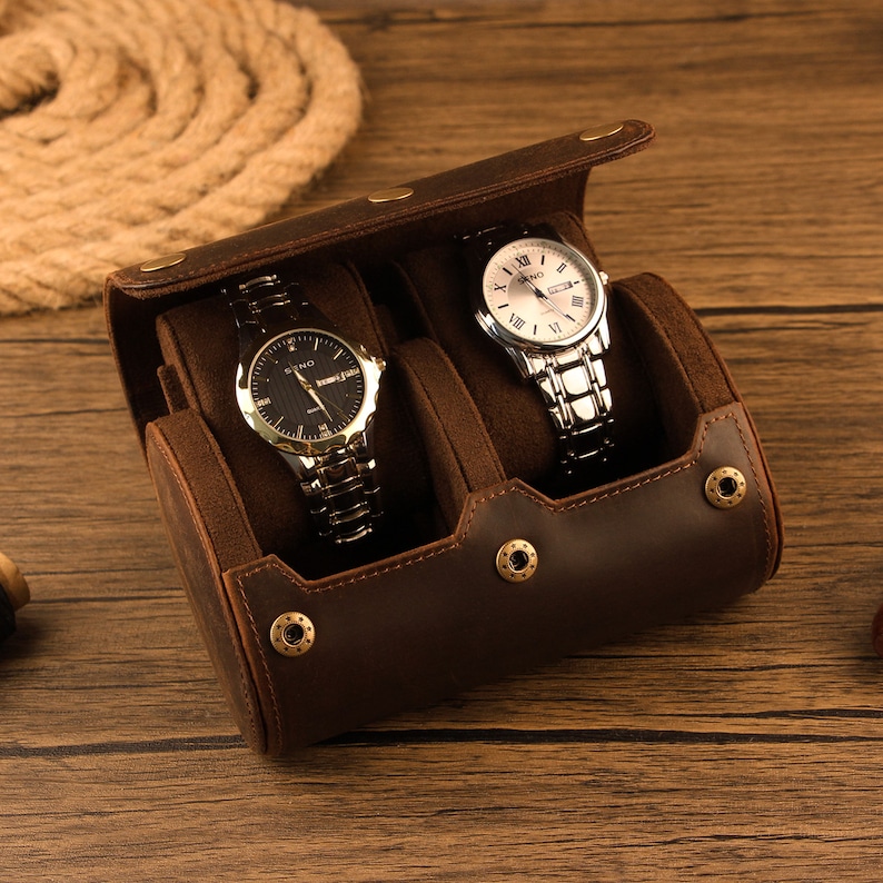 Peut inclure: Un enrouleur de montres en cuir marron avec deux montres &agrave; l'int&eacute;rieur. L'enrouleur de montres a un ext&eacute;rieur en cuir marron et un int&eacute;rieur en tissu marron doux. Les montres ont des bracelets argent&eacute;s et dor&eacute;s.
