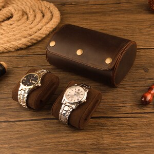 Peut inclure: Deux montres-bracelets avec des bracelets en m&eacute;tal sont pr&eacute;sent&eacute;es sur des coussins de montre en velours marron. Un porte-montres en cuir marron avec trois boutons pression en laiton est &eacute;galement pr&eacute;sent&eacute;.