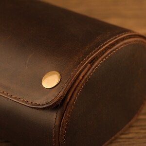 Peut inclure: Gros plan sur un porte-montres en cuir marron avec un bouton en m&eacute;tal dor&eacute;. Le rouleau est cousu avec du fil marron.
