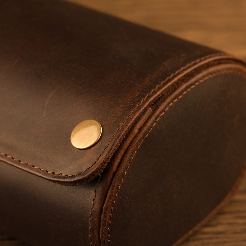 Peut inclure: Gros plan sur un porte-montres en cuir marron avec un bouton en m&eacute;tal dor&eacute;. Le rouleau est cousu avec du fil marron.