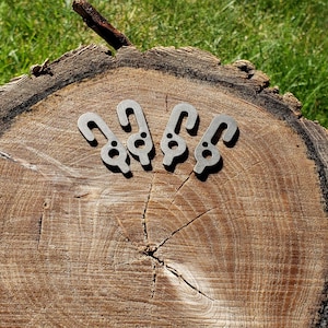 May include: Four metal bunny rabbit keyrings are displayed on a wooden tree stump. The keyrings are silver and have a minimalist design. The background is green grass, with the tree stump's rings visible.