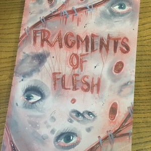 Puede incluir: Una pintura de acuarela de una portada de libro con el título "Fragments of Flesh" en letras rojas. La portada presenta varios ojos con costuras rojas y azules alrededor.