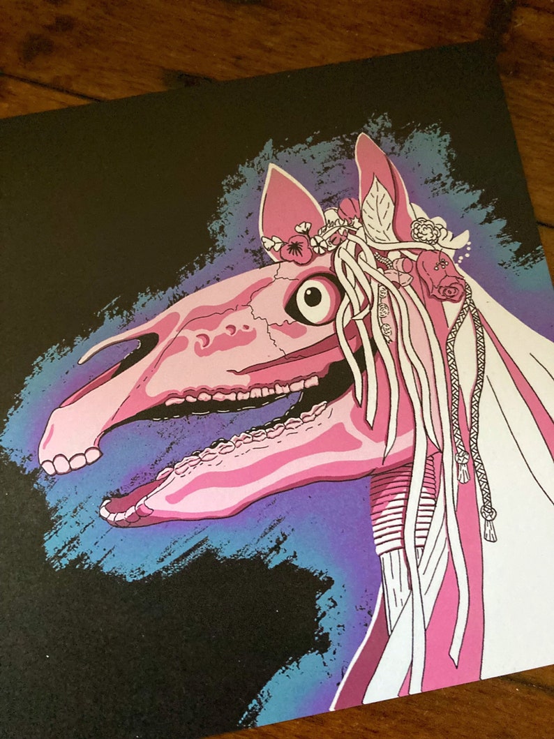 May include: A pink horse skull with a floral crown and white ribbons against a black background with blue and purple brushstrokes.