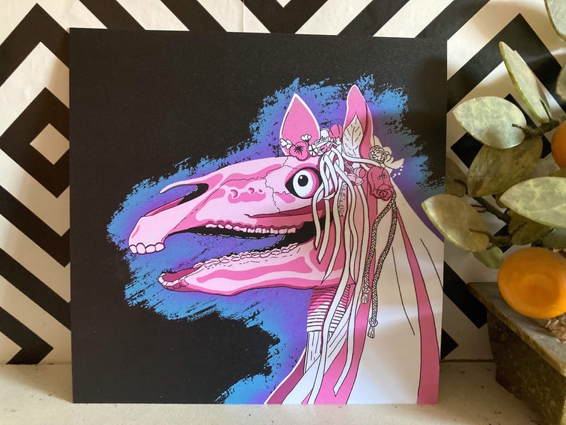 May include: A pink and white horse skull with a floral crown and a veil. The skull is set against a dark blue and purple background.