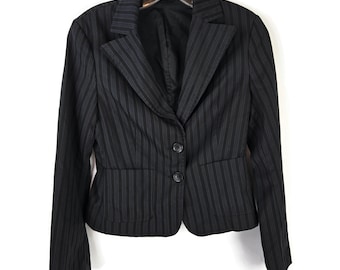 May include: A black blazer featuring thin, vertical grey pinstripes. The garment has a notched lapel, long sleeves, and a front closure secured by two black buttons. Two horizontal pockets are positioned at the waistline of the jacket.
