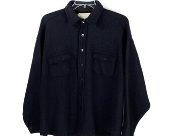 May include: A dark navy blue button-down shirt with two chest pockets. The shirt has a collar and is made of a thick, textured fabric. It is hanging on a white hanger against a white background.