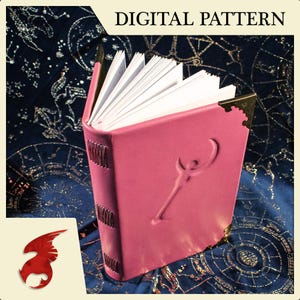 May include: A pink leather-bound journal with a gold embossed design of a crescent moon and a key. The journal is closed and has a decorative gold clasp.