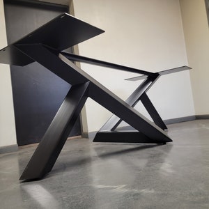 May include: Black metal table base with a geometric design. The base is made of thick, sturdy metal and has a black finish.