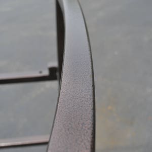 May include: Close-up of a curved metal railing with a textured, dark brown finish.