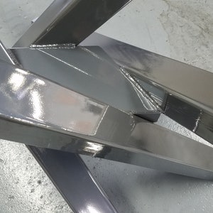 May include: Close-up of a metal frame with a shiny, gray paint finish. The frame is made of thick, rectangular metal bars that are welded together at the corners. The frame is angled and the metal is reflective.