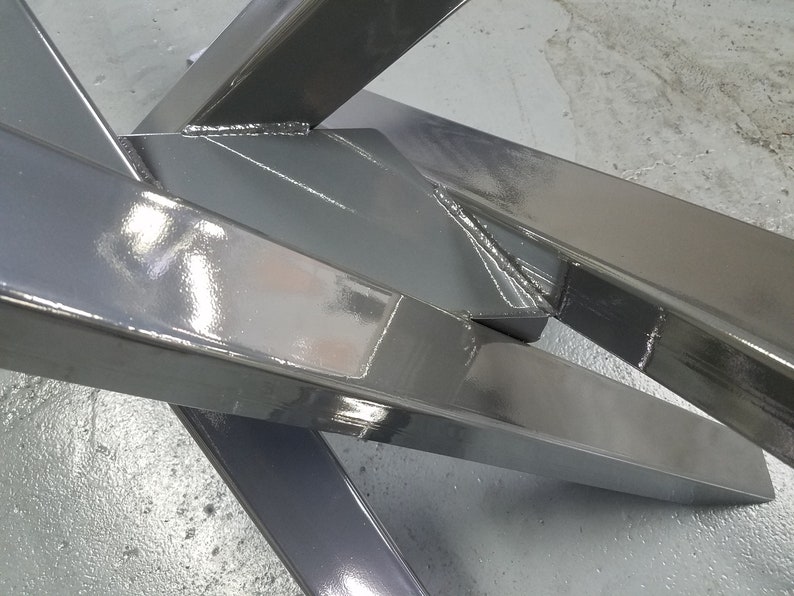May include: Close-up of a metal frame with a shiny, gray paint finish. The frame is made of thick, rectangular metal bars that are welded together at the corners. The frame is angled and the metal is reflective.