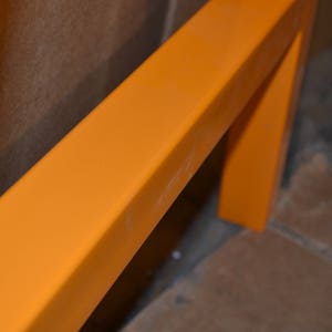 May include: Close-up of a bright orange metal frame. The frame is made of thick, rectangular metal bars. The frame is painted a vibrant orange color.
