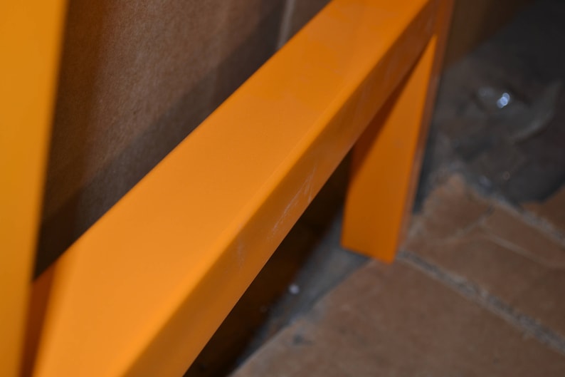 May include: Close-up of a bright orange metal frame. The frame is made of thick, rectangular metal bars. The frame is painted a vibrant orange color.