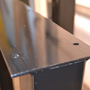May include: Black metal table leg with two screw holes on the top surface.