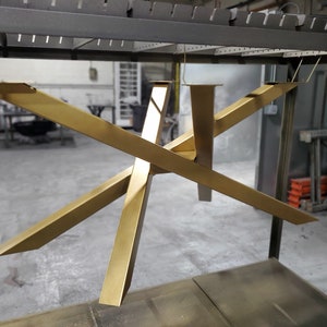 May include: Gold metal table base with a geometric design. The base is suspended from the ceiling by wires.