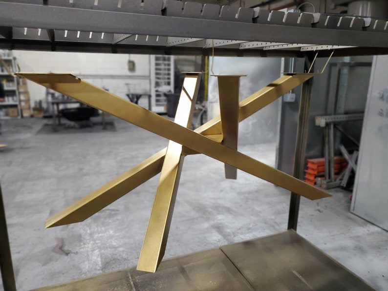 May include: Gold metal table base with a geometric design. The base is suspended from the ceiling by wires.