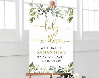 May include: A white sign with gold lettering that reads "baby in bloom" and "Welcome to Samantha's Baby Shower August 23, 2023". The sign is decorated with green watercolor leaves and is displayed on an easel.