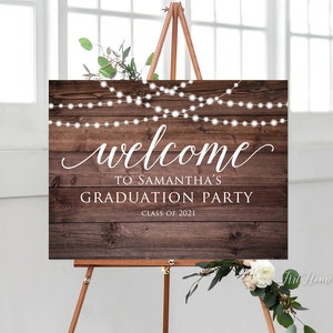 May include: A rustic wooden welcome sign with white string lights and the text "Welcome to Samantha's Graduation Party Class of 2021".