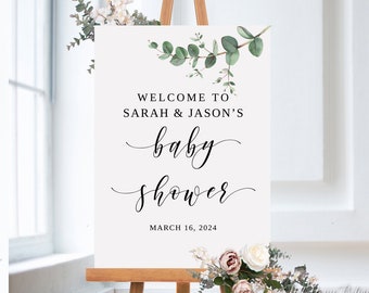 May include: White welcome sign with green eucalyptus leaves and the text "Welcome to Sarah & Jason's Baby Shower March 16, 2024".